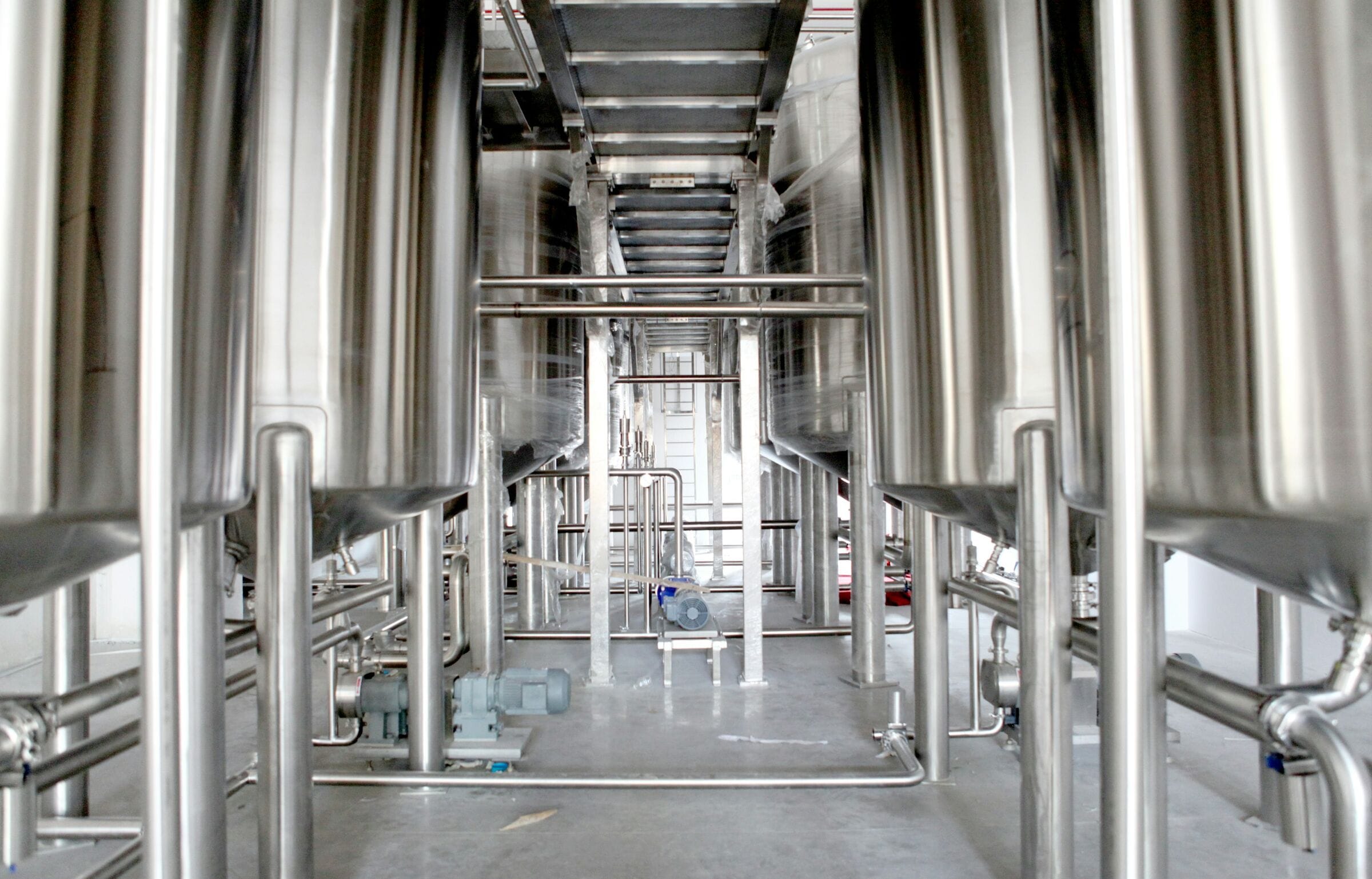 An aisle between tall stainless process tanks and pipework in a large production hall
